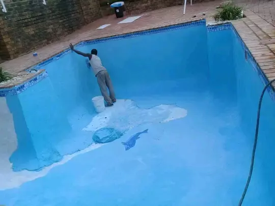 A worker painting the interior of an empty swimming pool